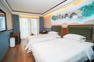 Habitación de hotel con dos camas, un escritorio, una silla, un cesto de basura y un ventanal con cortinas.