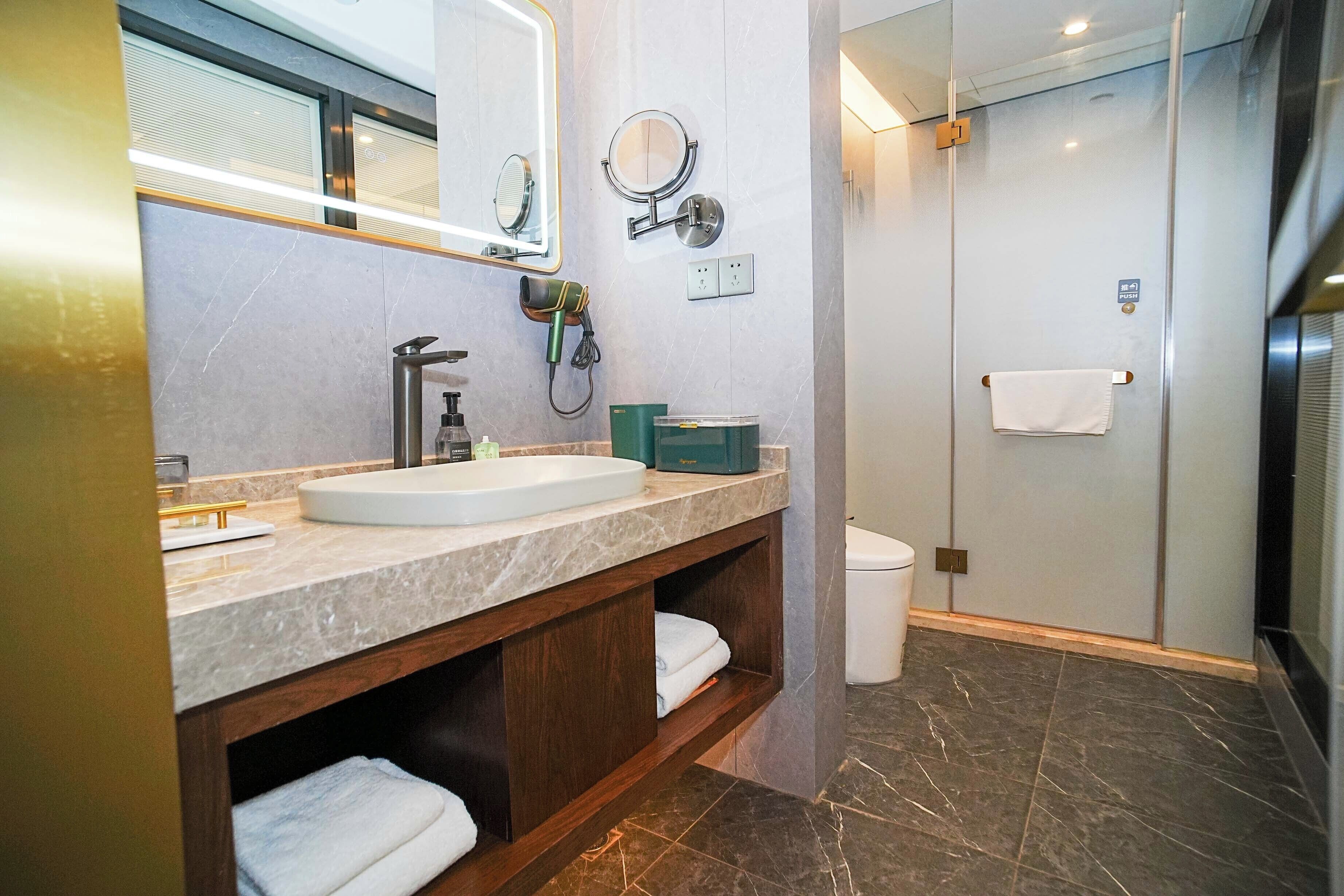 A modern bathroom with a marble vanity, a hairdryer, a towel rack, and a glass-enclosed shower.