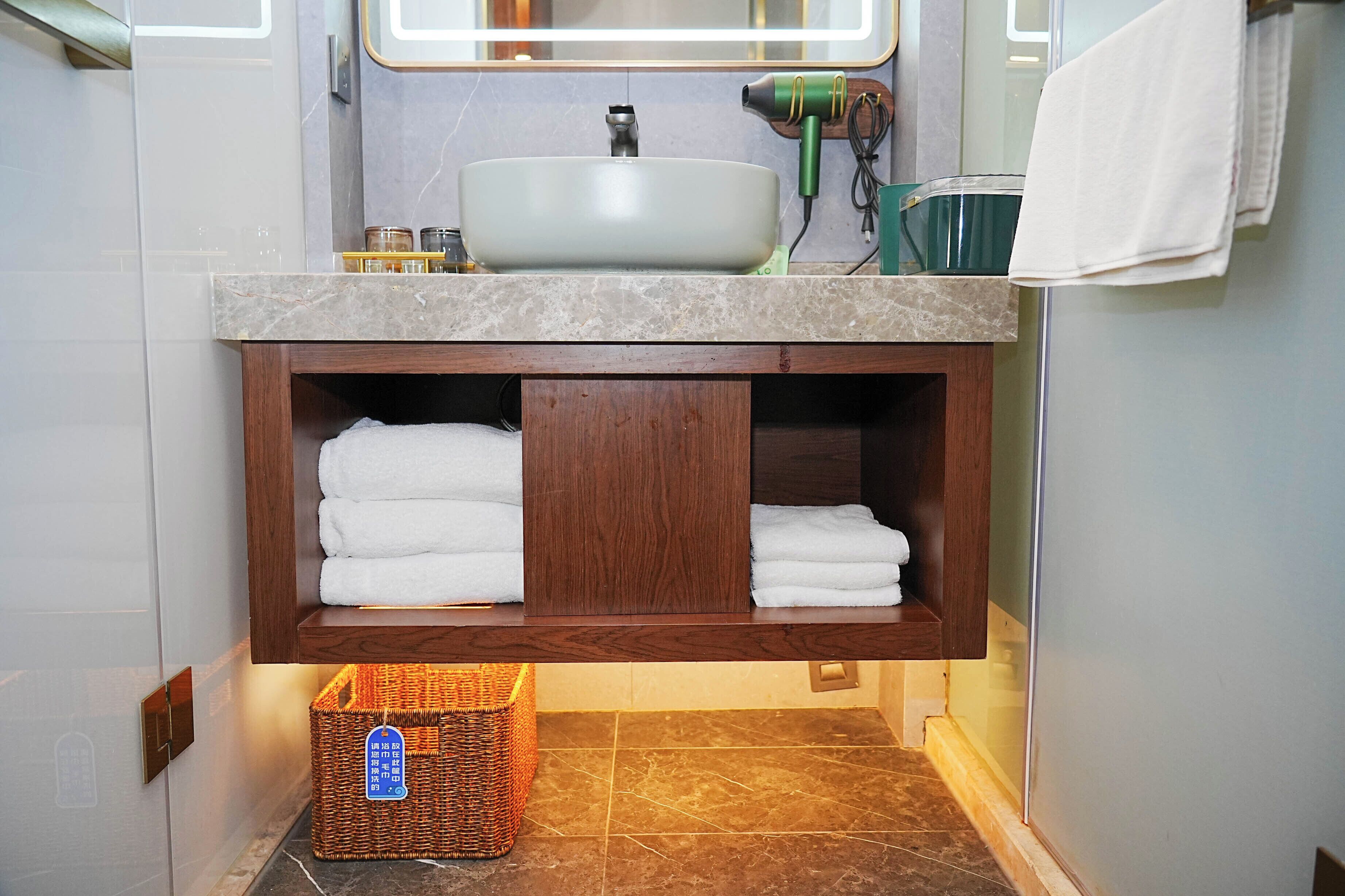 Un baño con encimera de mármol, un lavabo, un secador de pelo y toallas ordenadas en estantes.