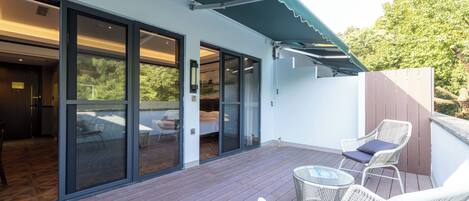 A modern outdoor patio with a wooden deck, large sliding glass doors leading to a room, and wicker furniture.