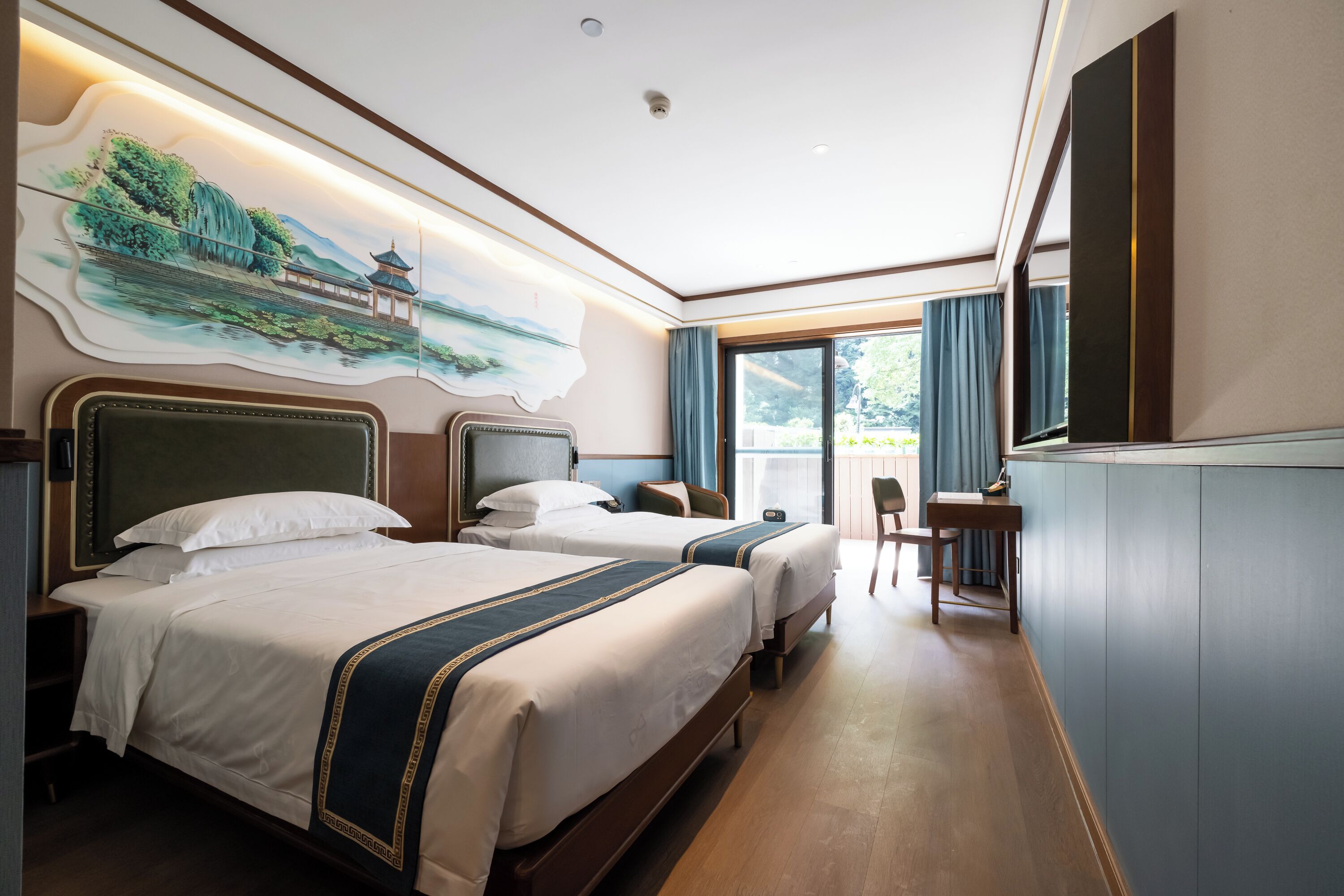 A hotel room with two beds, a desk, a chair, and a large window with curtains.