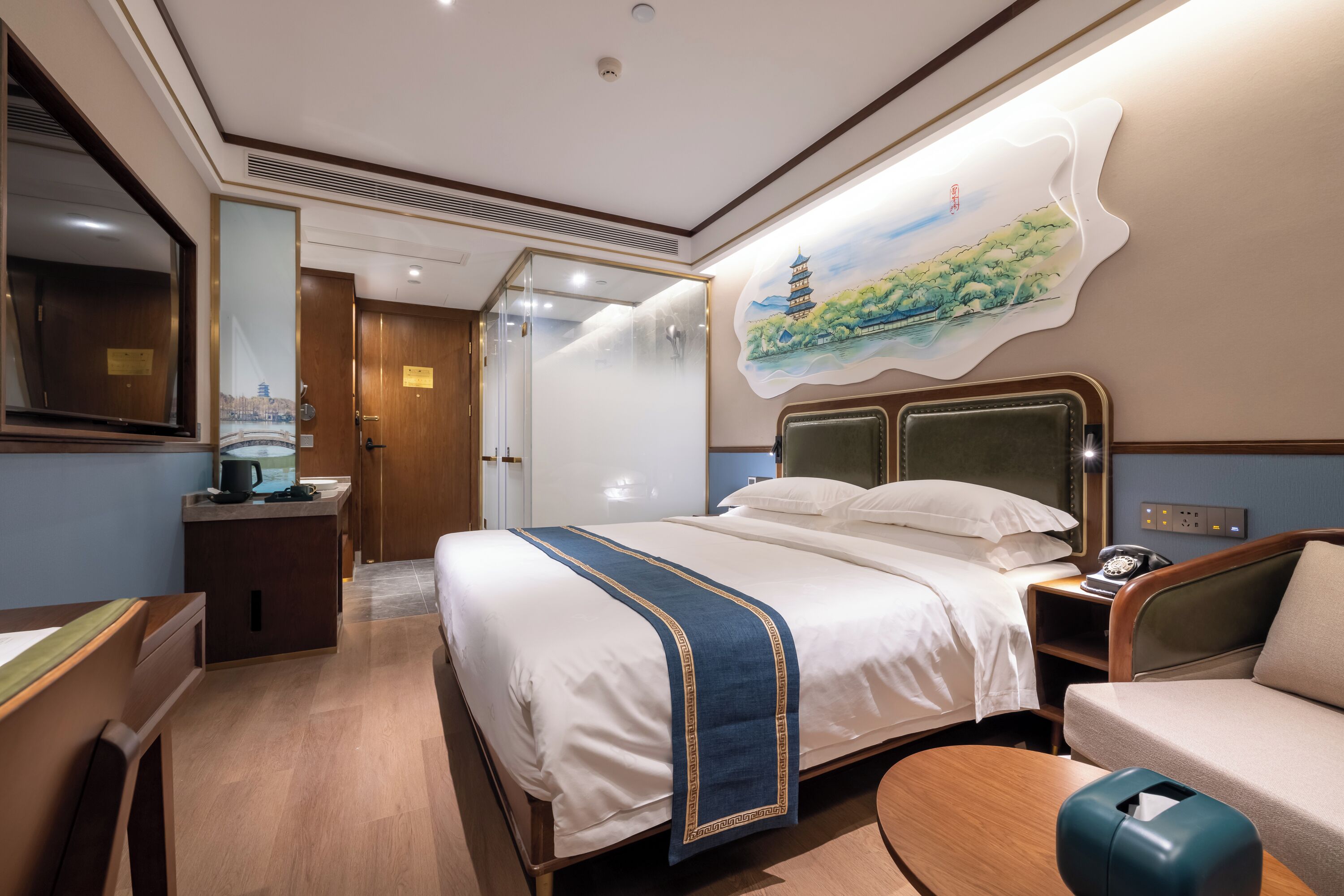 A hotel room with a large bed, a desk, a chair, a sofa, and a painting on the wall.