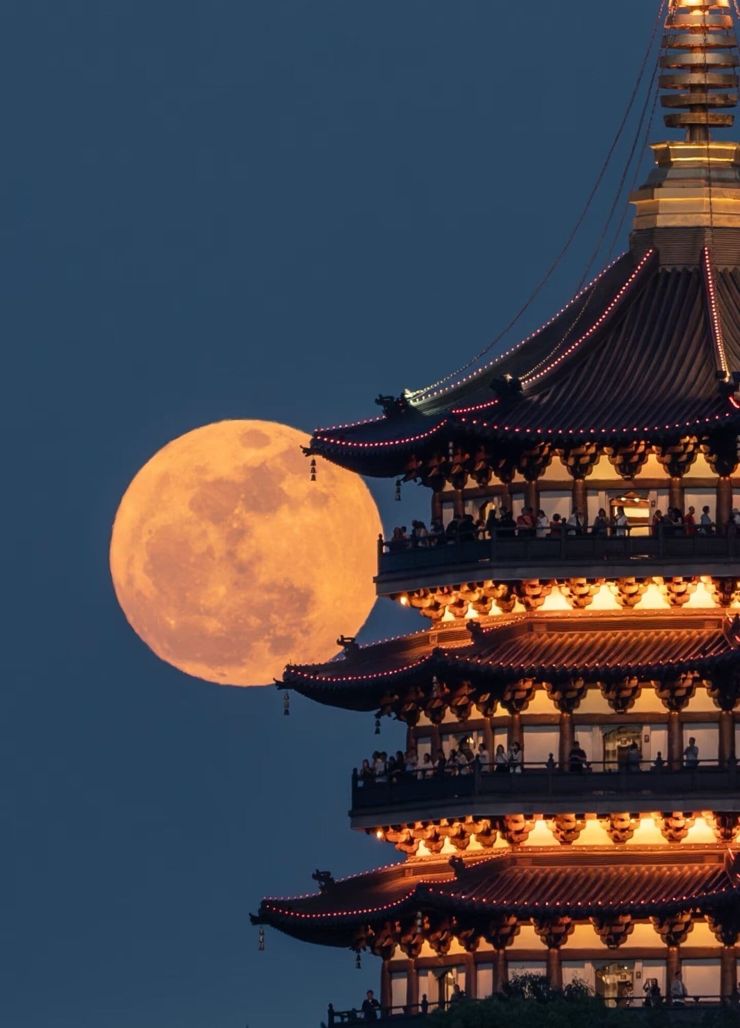 A traditional multi-tiered pagoda with illuminated railings and a full moon in the background.
