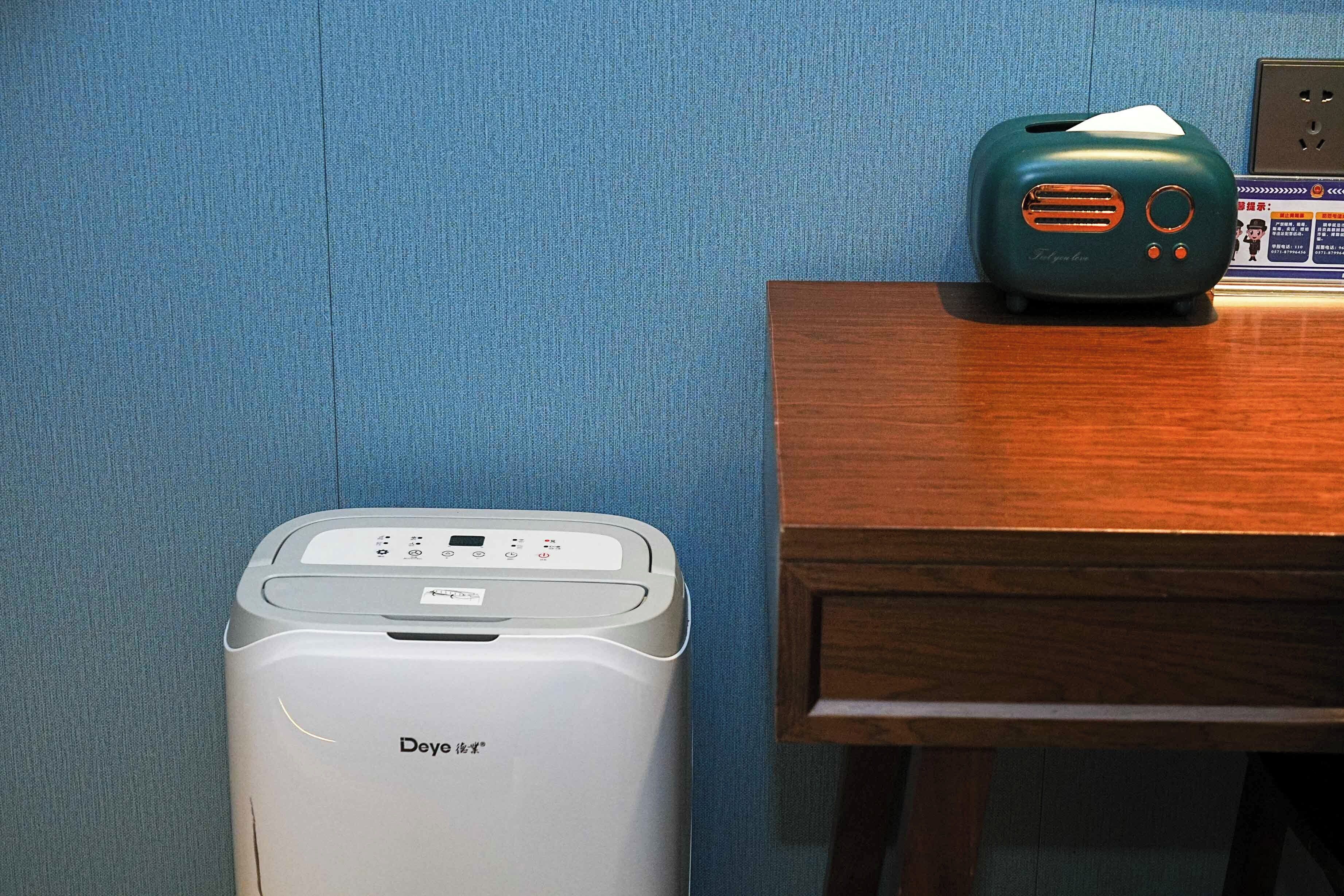 A De'Longhi air purifier and a vintage radio on a wooden table against a blue wall.