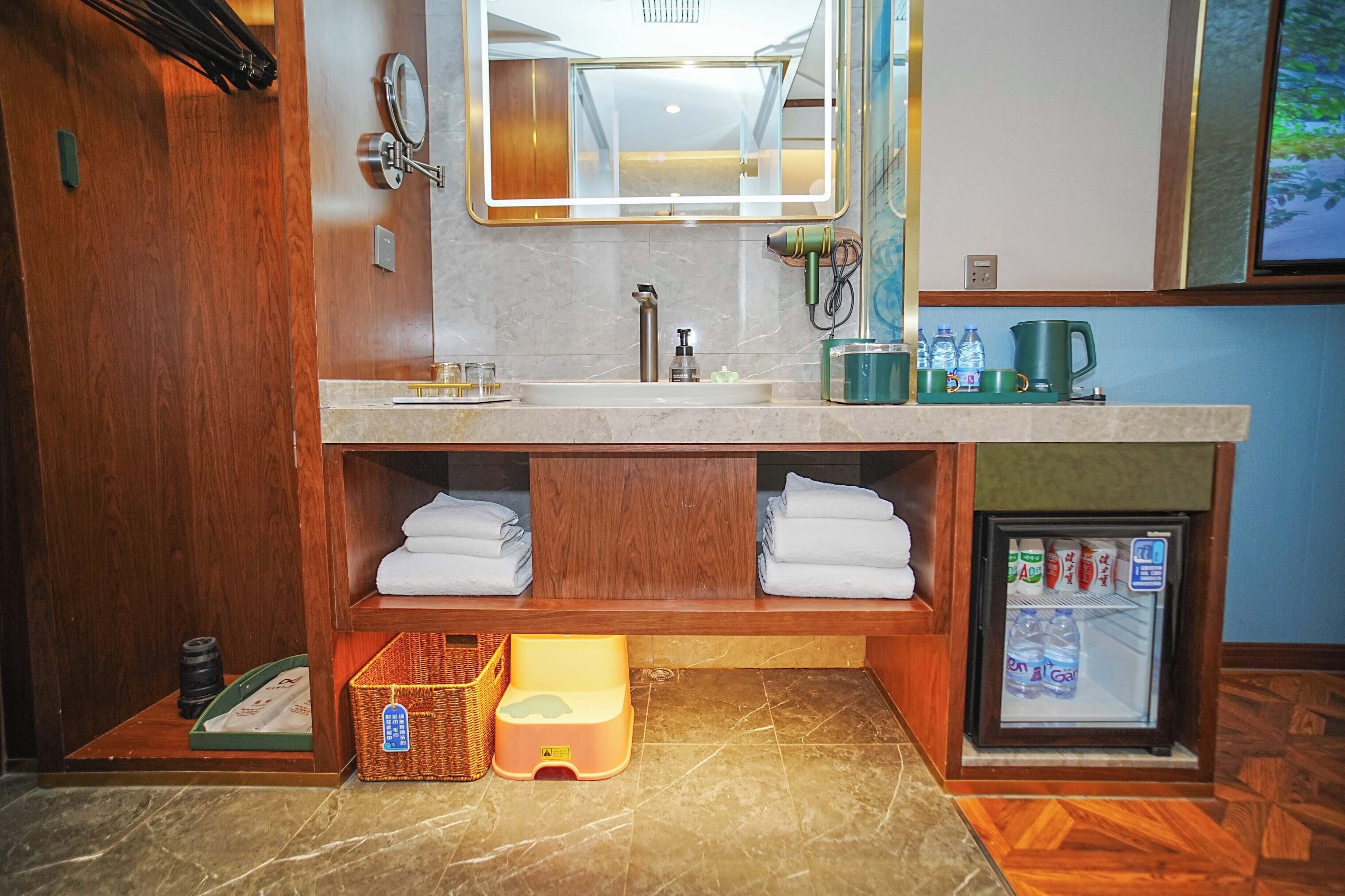A bathroom with a double sink, a mirror, a towel rack, a small refrigerator, and a wooden vanity.