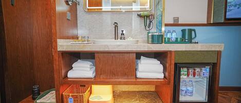 Un baño con lavamanos doble, un espejo, toallero, refrigerador pequeño y tocador de madera.