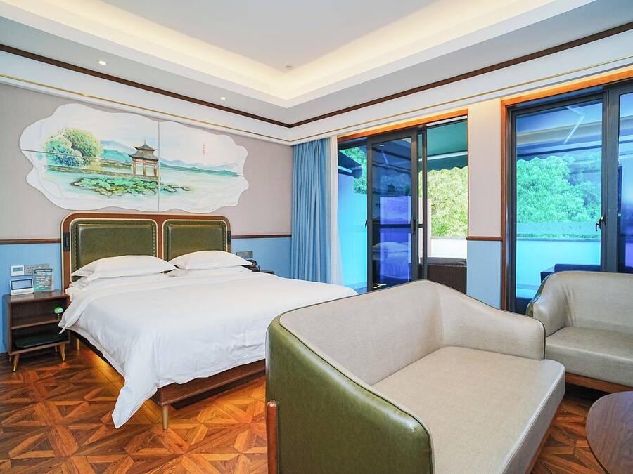 A hotel room with a bed, a chair, a desk with a computer, and a painting on the wall.