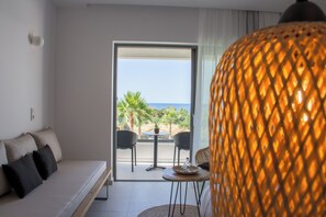 A modern hotel room with a sofa, a dining table, and a view of the ocean through a glass door. - Aqua Blu (Hersonissos)