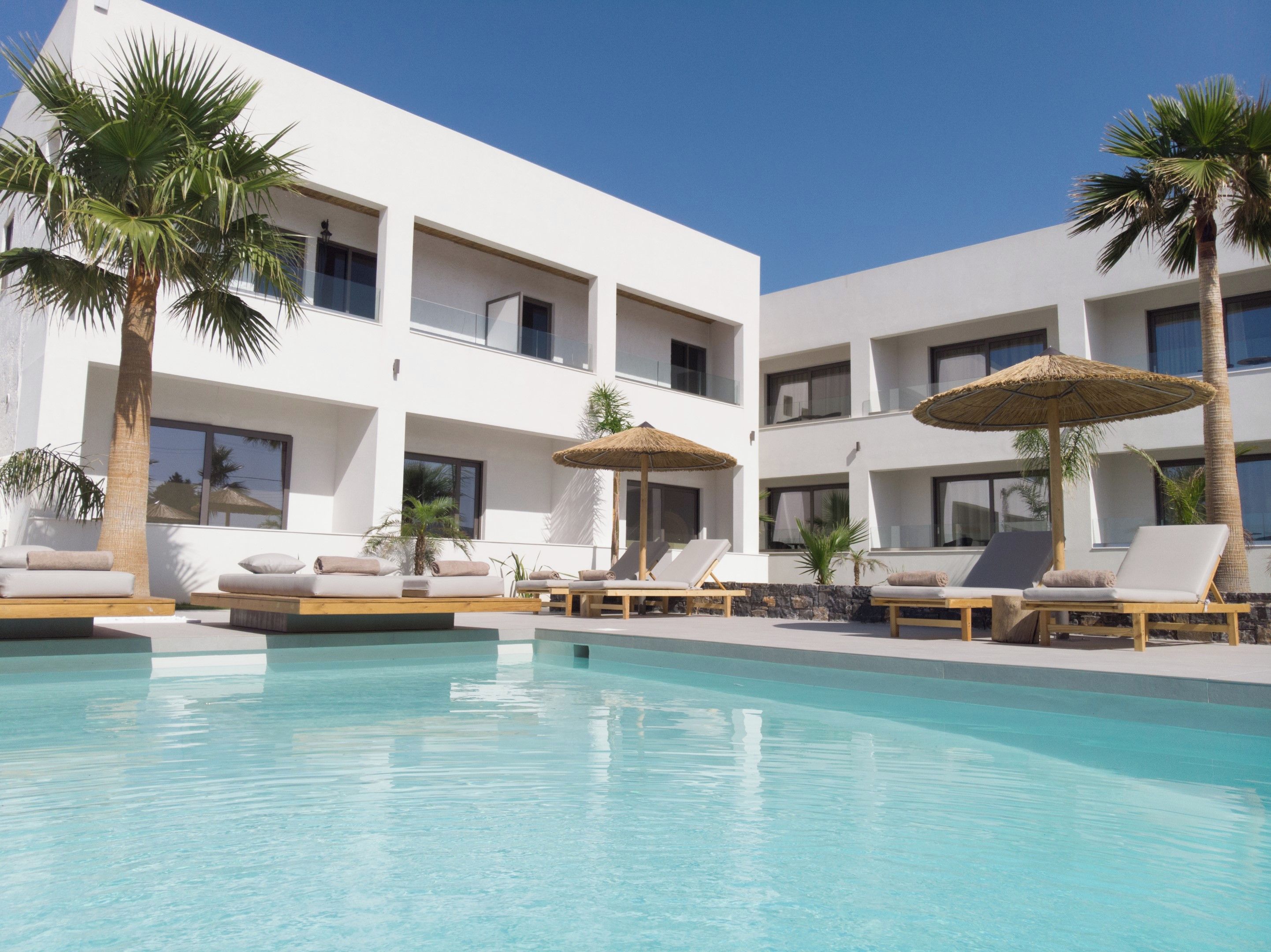 A modern hotel with a pool area, sun loungers, and palm trees.