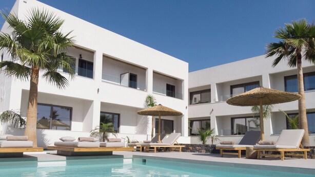Un hôtel moderne doté d’une piscine, de chaises longues et de palmiers.