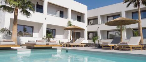 A modern hotel with a pool area, sun loungers, and palm trees.