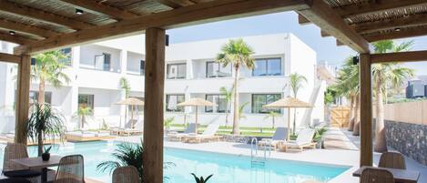 An outdoor pool area with lounge chairs, a wooden deck, and a view of a modern building.