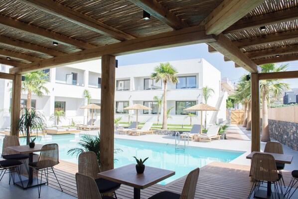 An outdoor pool area with lounge chairs, a wooden deck, and a view of a modern building. - Aqua Blu (Hersonissos)