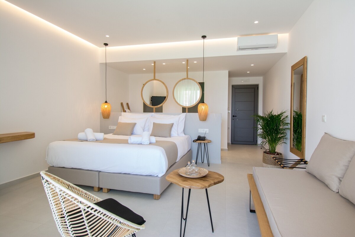 A modern hotel room with a large bed, bedside tables, a sofa, a chair, and a mirror.