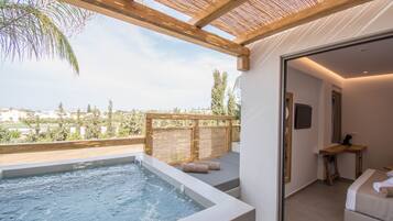 Een wellnessruimte met een jacuzzi, een houten terras en een slaapkamer met een bed en bureau.