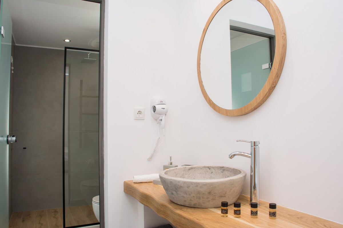 A bathroom with a large oval mirror, a stone sink, and a handheld hair dryer on the wall.