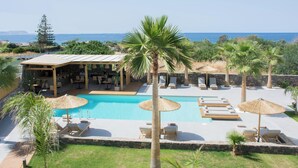A pool area with lounge chairs and umbrellas, a bar area, and a view of the sea. - Aqua Blu (Hersonissos)