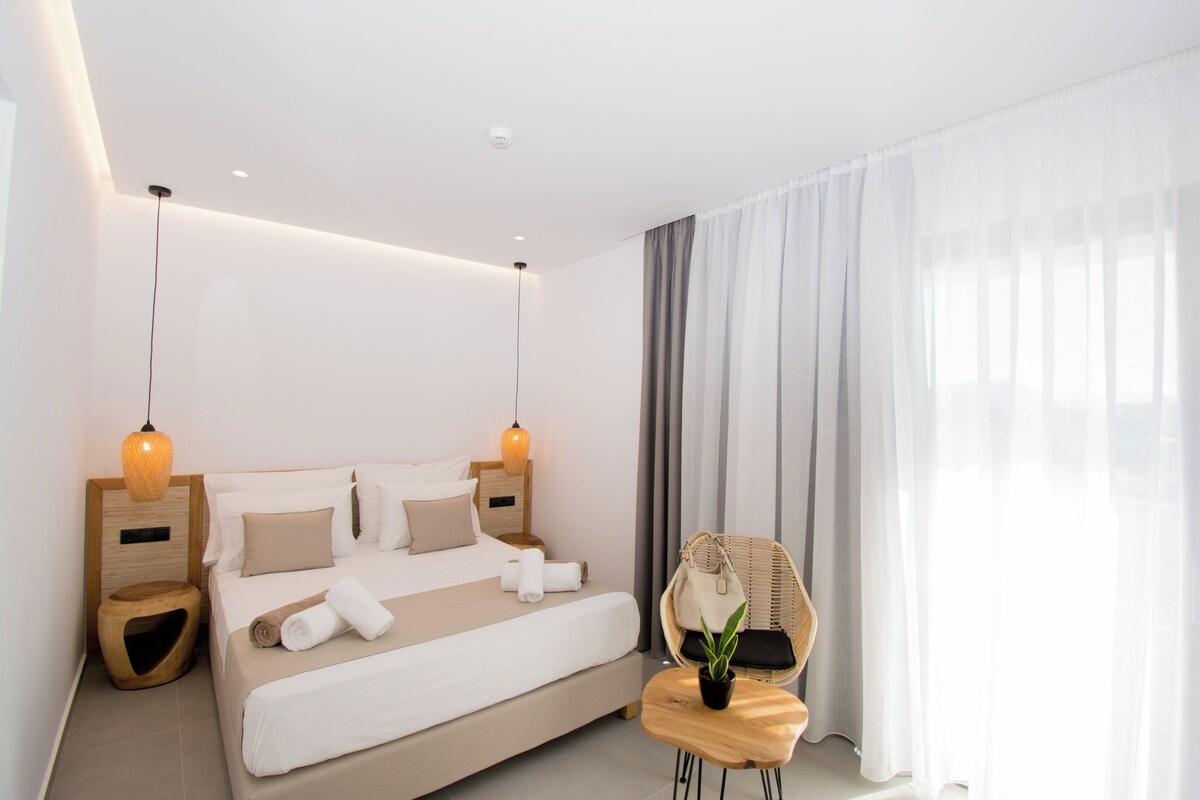Une chambre d’hôtel moderne avec un grand lit, deux tables de chevet, une chaise et une plante en pot.