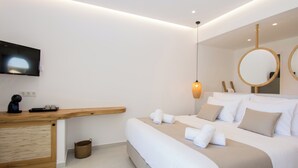 Une chambre d’hôtel moderne avec un bureau en bois, un téléviseur à écran plat, un lit avec du linge de maison blanc et deux miroirs ronds.