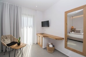 A modern hotel room with a wooden desk, a flat-screen TV, a bed, a wicker chair, and a potted plant. - Aqua Blu (Hersonissos)