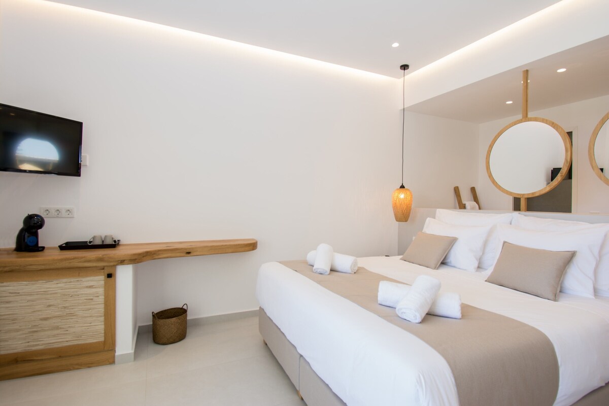 A modern hotel room with a wooden desk, a flat-screen TV, a bed with white linens, and two round mirrors.