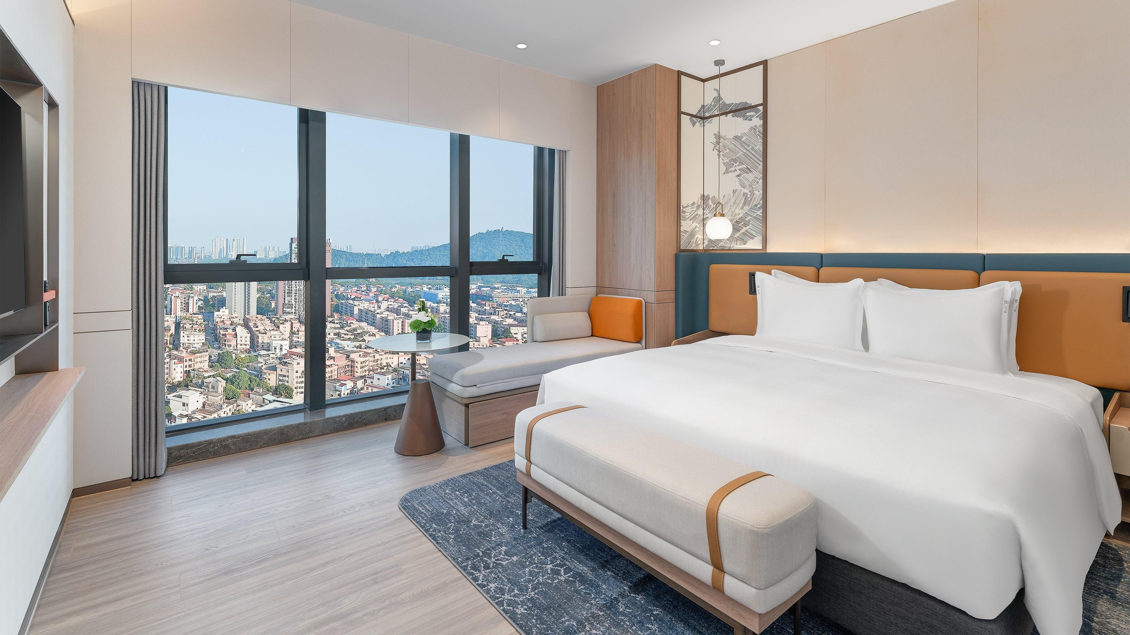 Una habitación de hotel moderna con una cama grande, un área de descanso y vistas a la ciudad.