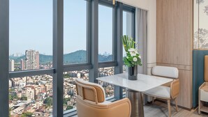 A modern room with a large window offering a city view, a small table with a vase of flowers, and a comfortable chair. - Holiday Inn Express Shunde Daliang (Foshan)