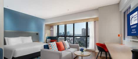 A modern hotel room with a bed, sofa, and a small dining table.
