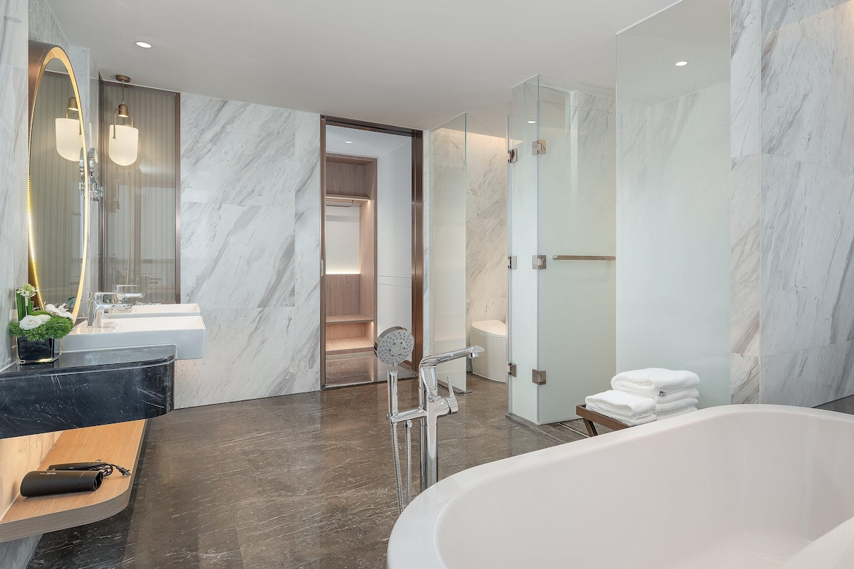 A modern bathroom with a marble floor, a freestanding bathtub, and a large mirror with a curved frame.