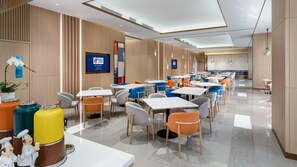 A modern hotel lobby with a long reception desk, multiple seating areas with tables and chairs, and a large screen displaying the hotel name. - Holiday Inn Express Shunde Daliang (Foshan)