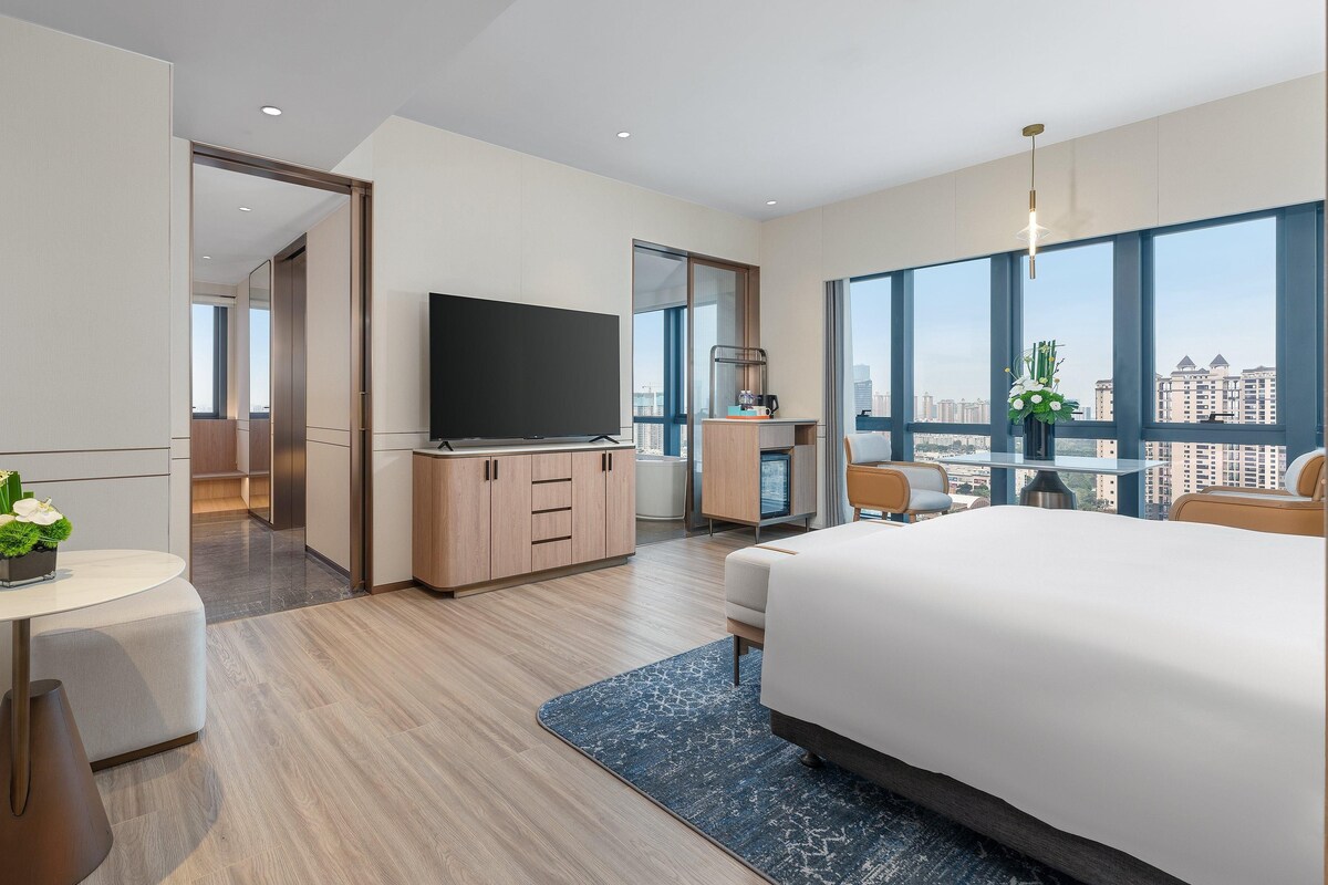 Ein modernes Hotelzimmer mit einem großen Bett, einem Fernseher, einem Schreibtisch und Blick auf die Stadt.
