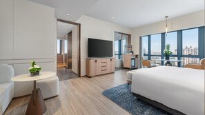 A modern hotel room with a large bed, a TV, a desk, and a view of the city.