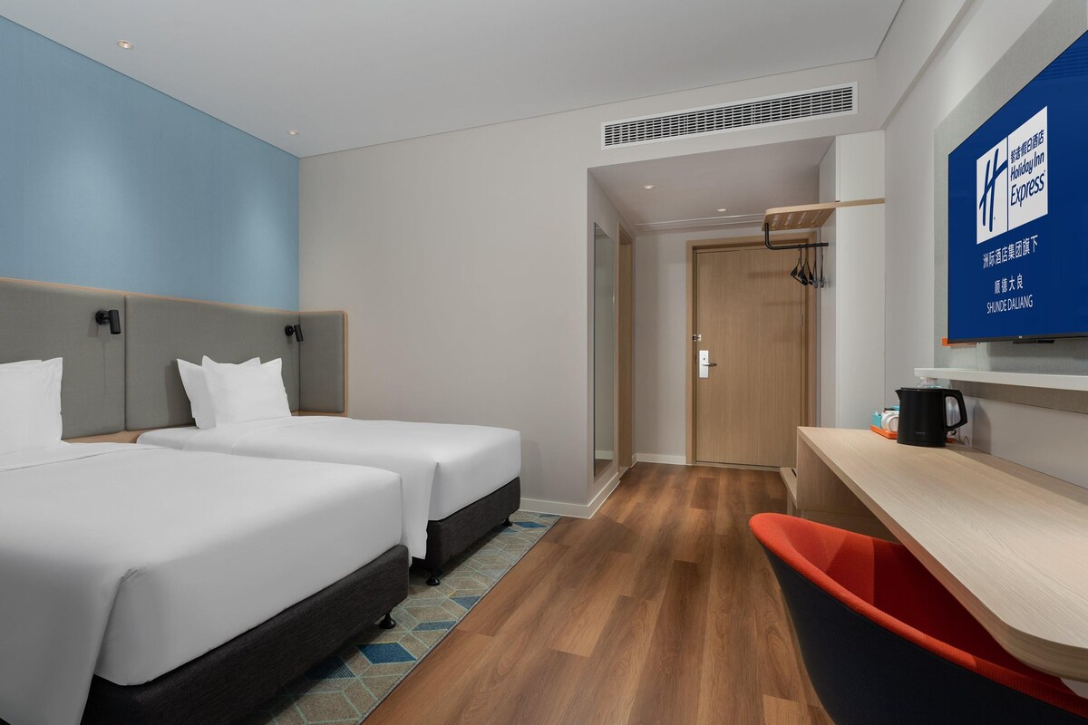 A hotel room with two beds, a desk, a chair, and a television on the wall.