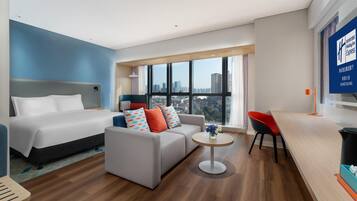 A modern hotel room with a bed, sofa, and dining area.