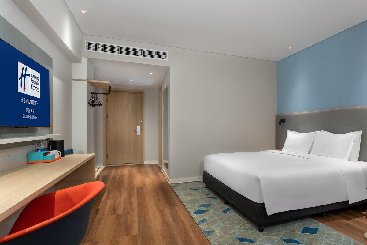 Ein Hotelzimmer mit Bett, Schreibtisch, Stuhl, Fernseher und einer Wandlampe.
