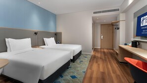 Two single beds with white linens and a wooden headboard, a desk and chair, and a flat-screen TV.