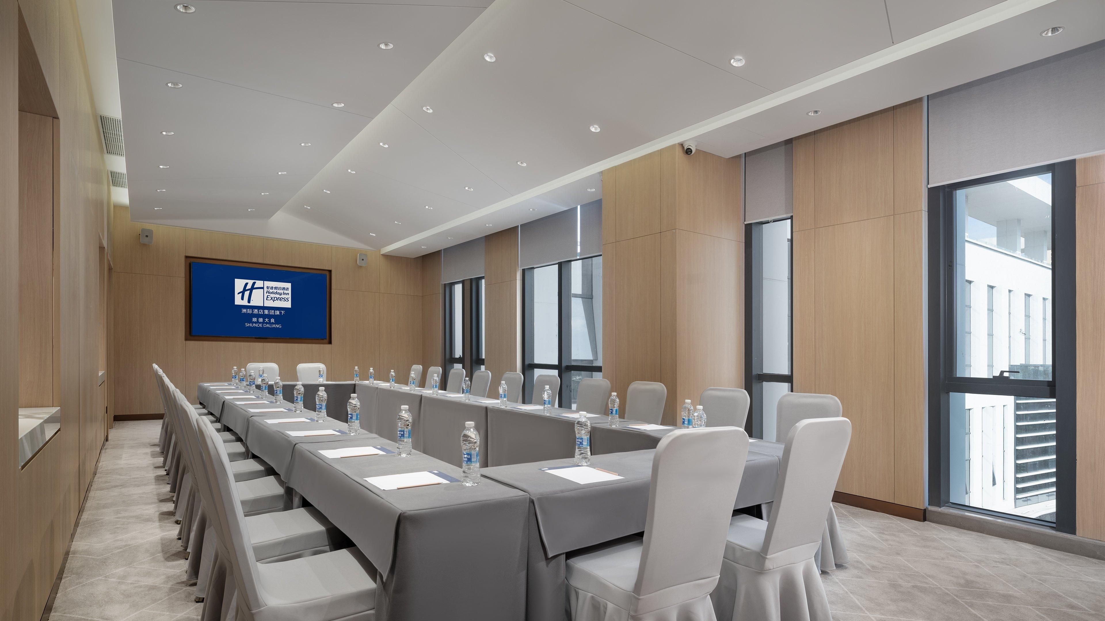A conference room with a long table, chairs, and a large screen displaying a logo.