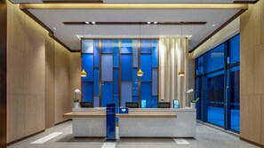 A modern reception desk with a blue patterned backdrop, two pendant lights, and a digital display.