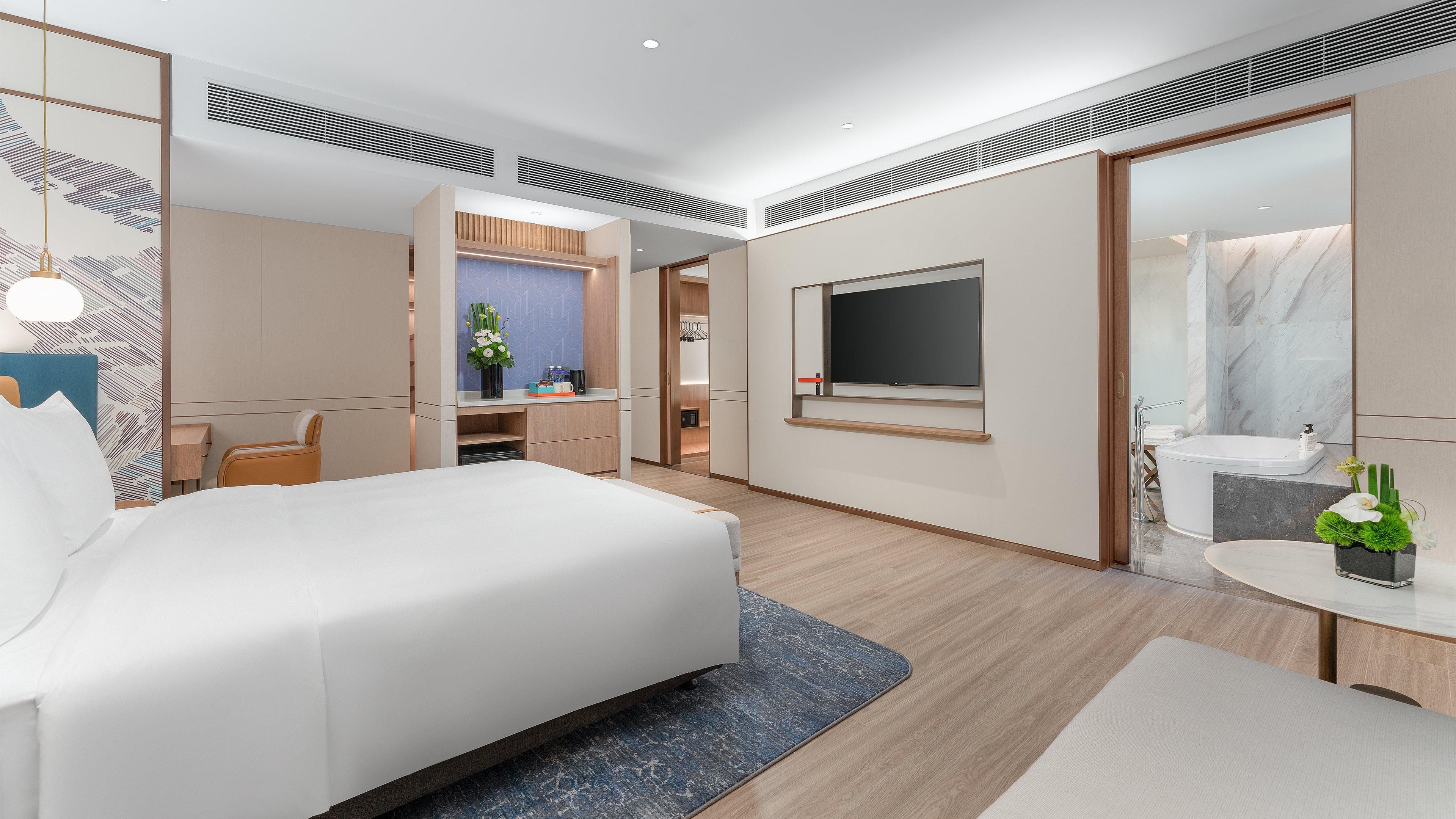 Una habitación de hotel moderna con una cama grande, un escritorio, un televisor y un baño con bañera y espejo.