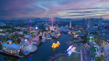 A waterfront amusement park with a Ferris wheel, a tall illuminated tower, and a stage area with a large screen.