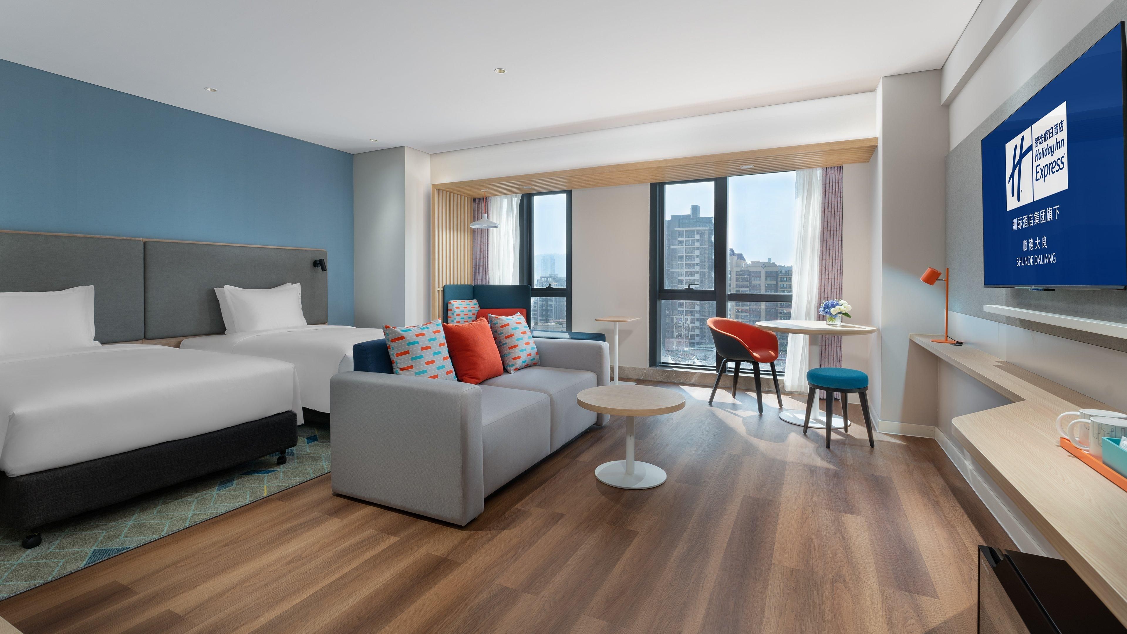 Une chambre d’hôtel moderne équipée de deux lits, d’un canapé, d’une petite table et d’un téléviseur.
