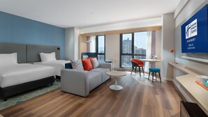 Una habitación de hotel moderna con dos camas, un sofá, una mesita y un televisor.