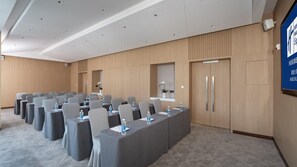 A conference room with rows of tables, chairs, and water bottles, featuring a wooden panel wall and a large screen on the right. - Holiday Inn Express Shunde Daliang (Foshan)