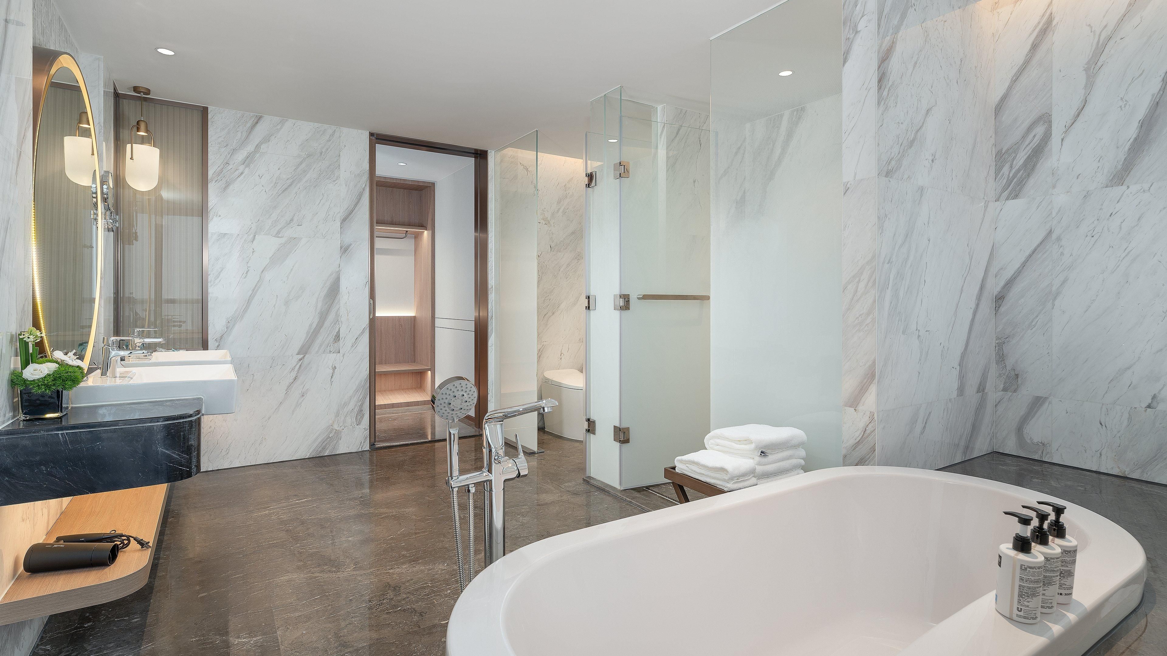 Un baño moderno con suelo de mármol, una bañera independiente y un espejo grande con marco curvo.