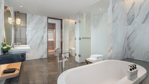 Un baño moderno con suelo de mármol, una bañera independiente y un espejo grande con marco curvo.