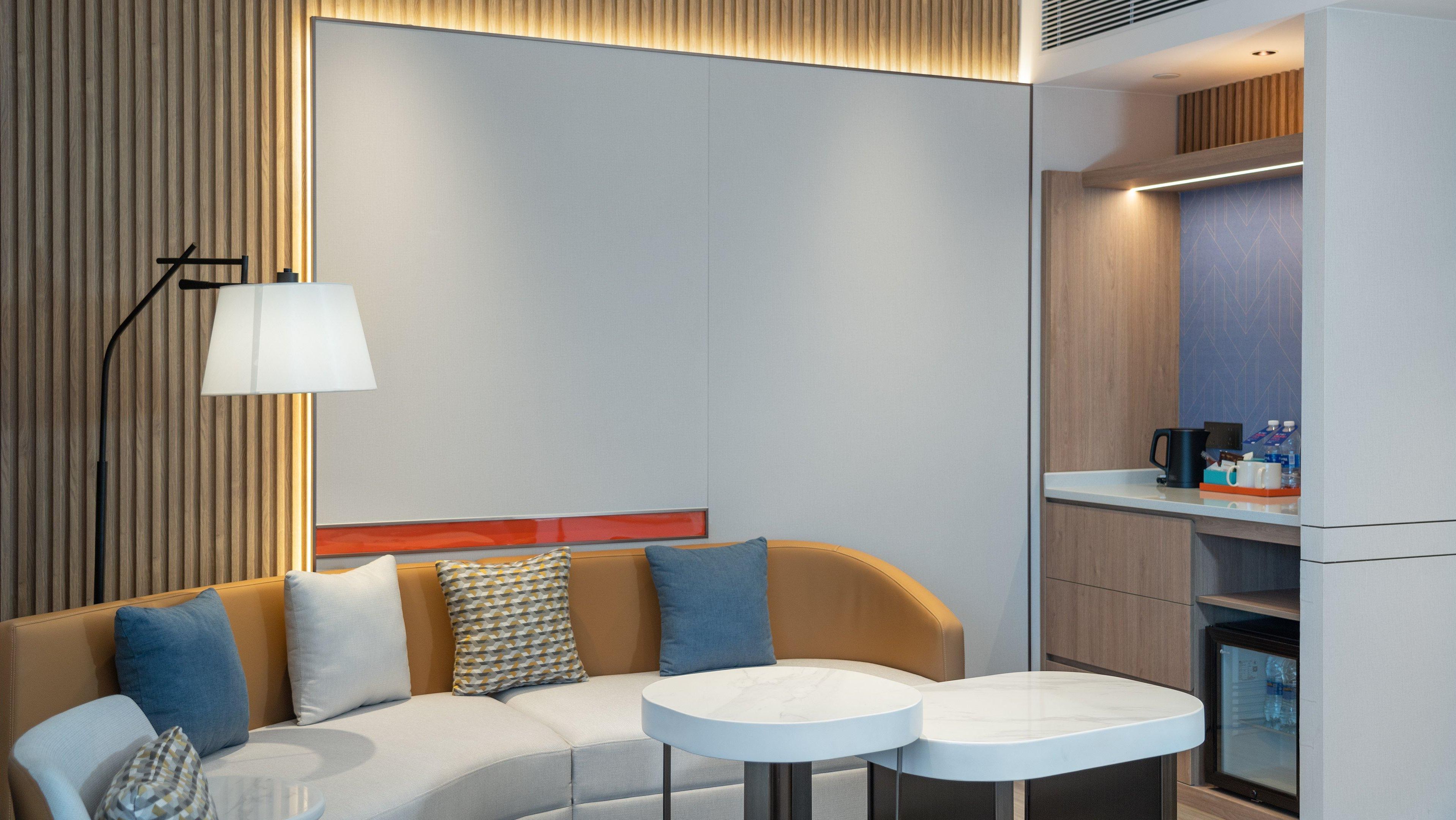 A modern living room with a sofa, two round tables, a lamp, and a kitchen area with a refrigerator.