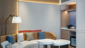 A modern living room with a sofa, two round tables, a lamp, and a kitchen area with a refrigerator. - Holiday Inn Express Shunde Daliang (Foshan)