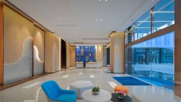 A modern hotel lobby with a reception desk, seating area, and a view of the pool.