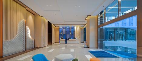A modern hotel lobby with a reception desk, seating area, and a view of the pool.