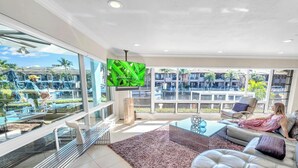 Amplio salón con televisor grande, asientos cómodos y vista a una piscina y edificios.